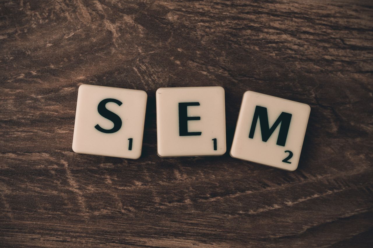 Fond en bois avec des lettres en relief formant SEM, illustrant le marketing sur les moteurs de recherche.